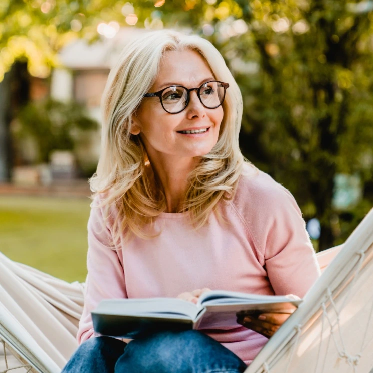 mature woman using reading glasses to read her book
