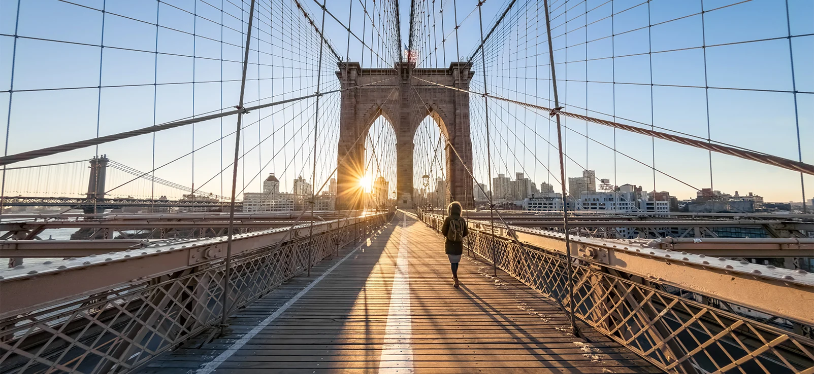 person walking on Brooklyn bridge at sunset