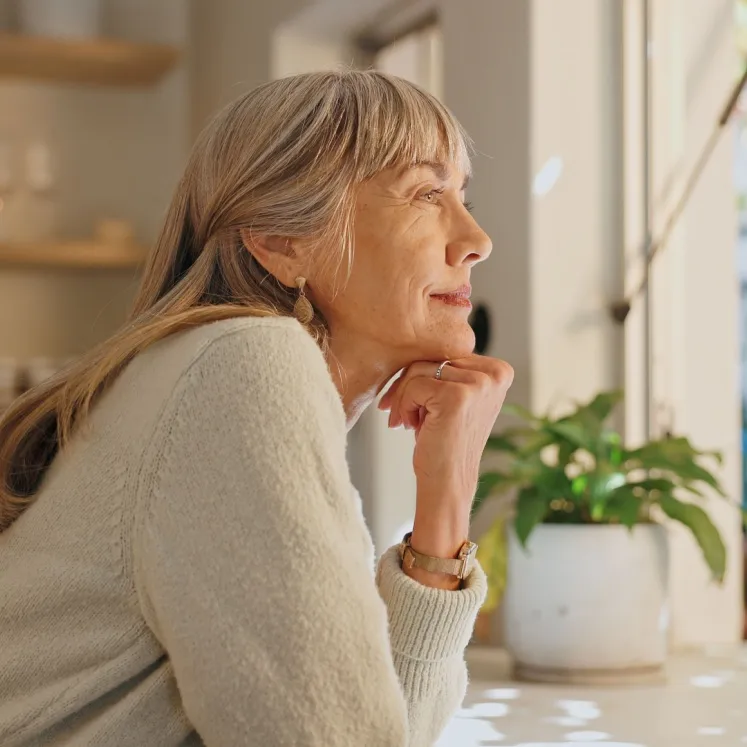 senior woman looking out kitchen window thinking