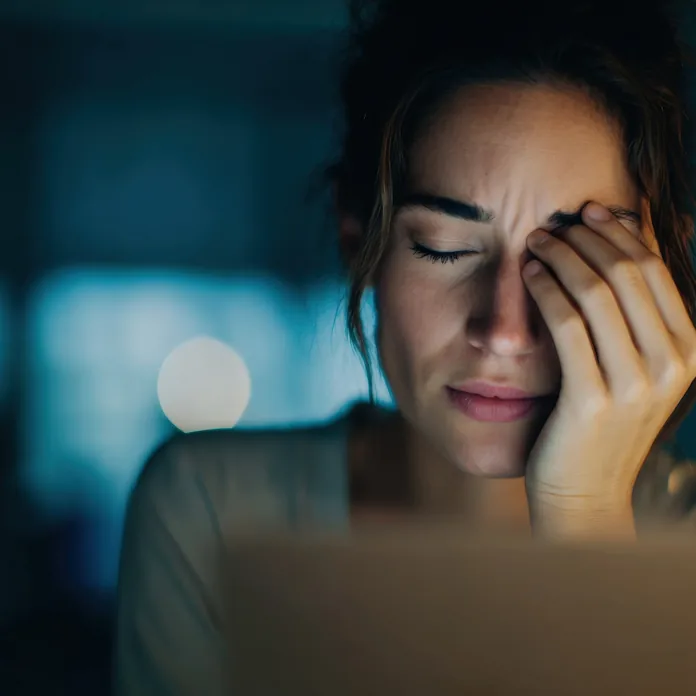 woman holding her face in pain from dry eyes caused by too much screen time
